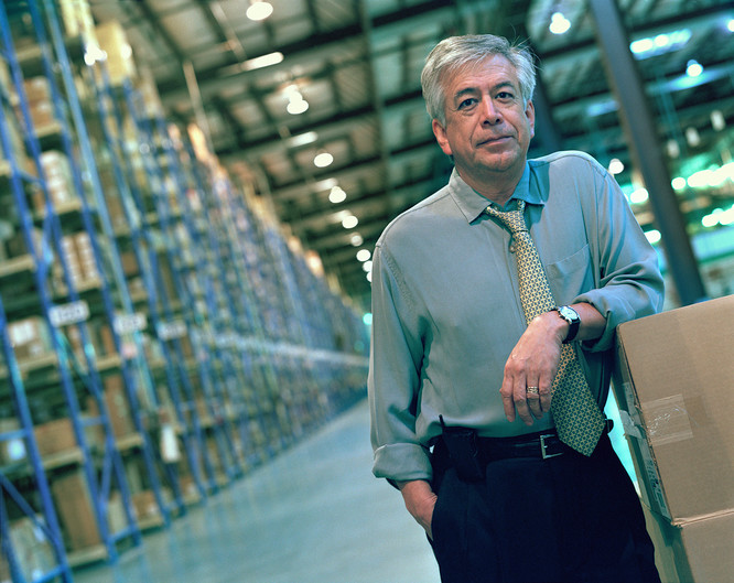 Businessman leaning on stack of boxes in warehouse, portrait